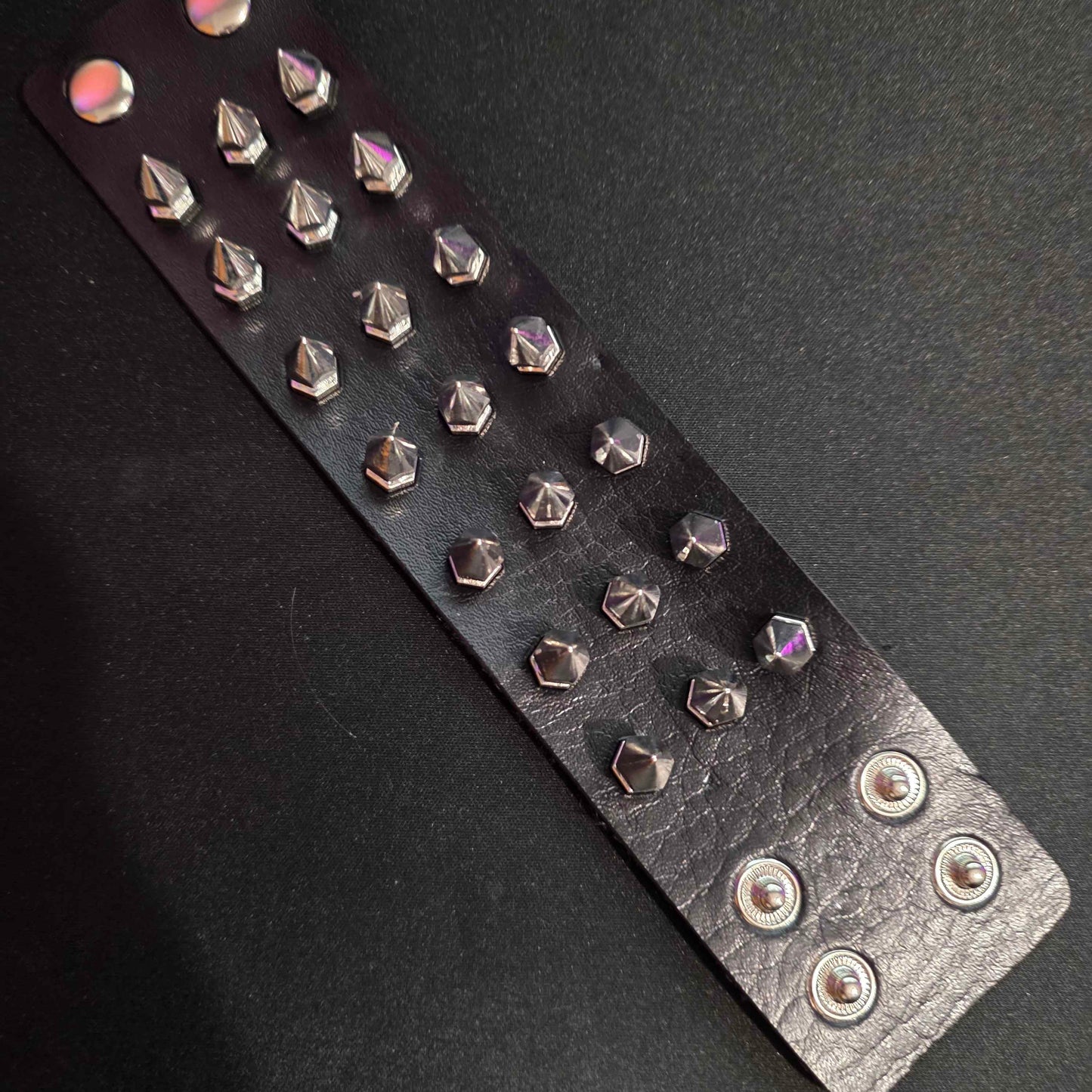 Black leather bracelet with silver studs on a dark background
