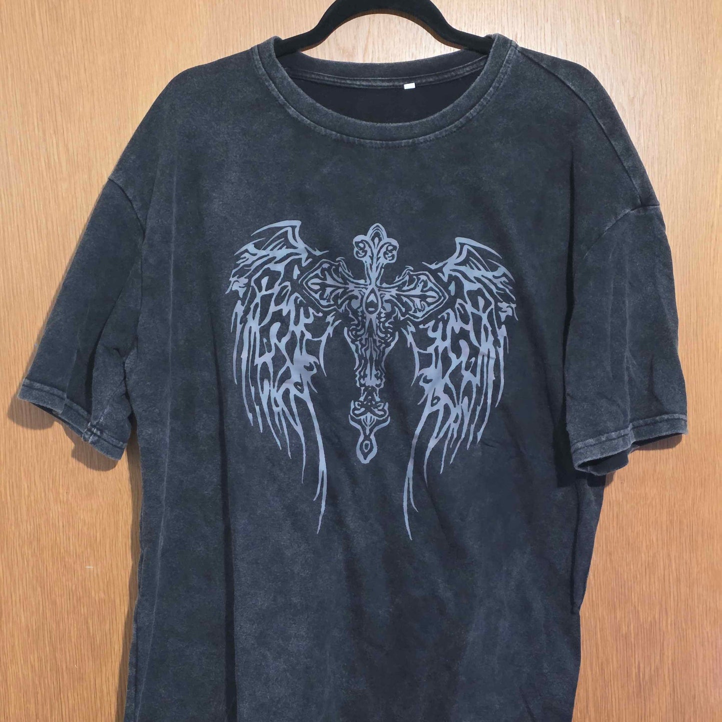 Black t-shirt with angel wings design on a wooden surface