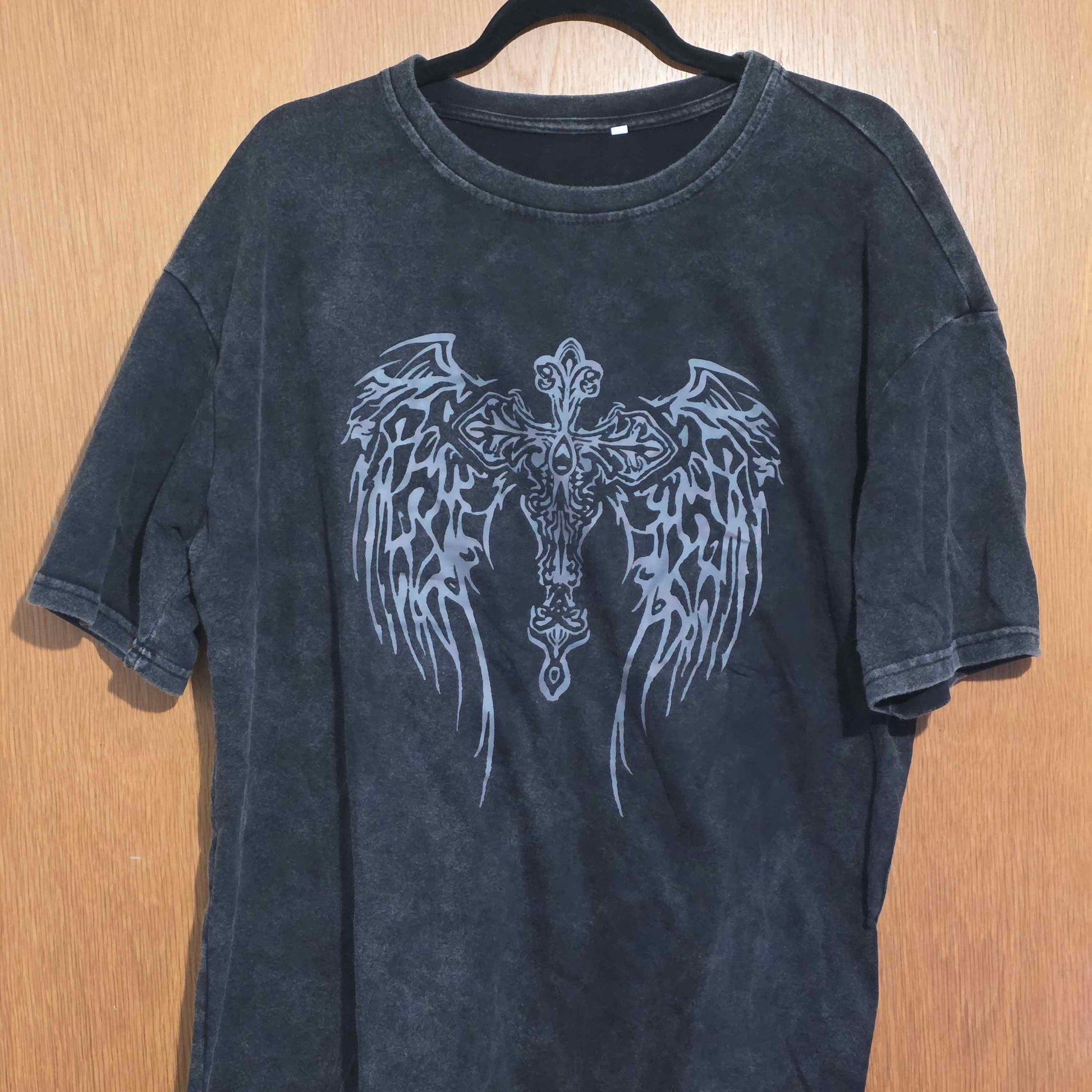 Black t-shirt with angel wings design on a wooden surface