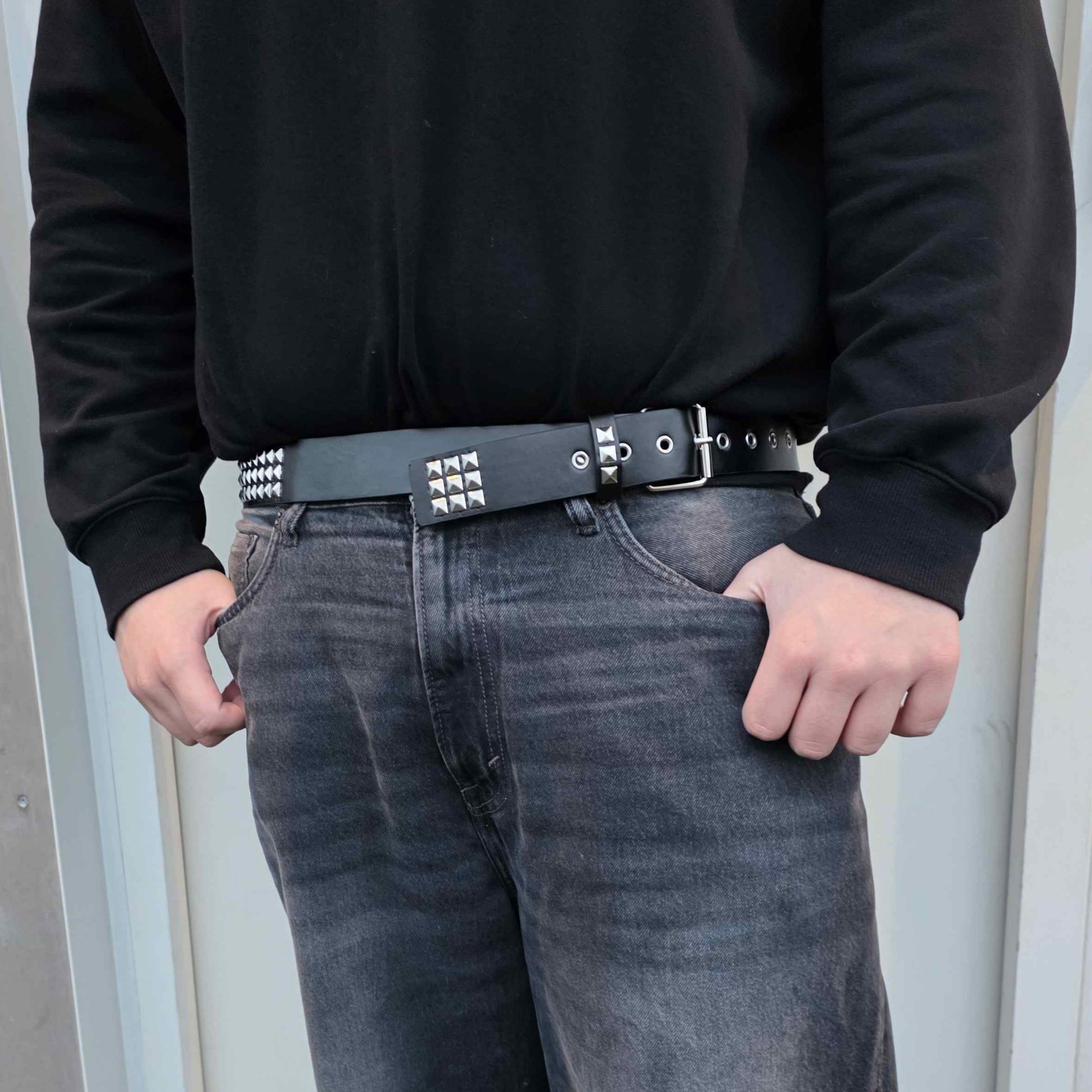 Person wearing a black sweater and gray jeans standing in front of a door.
