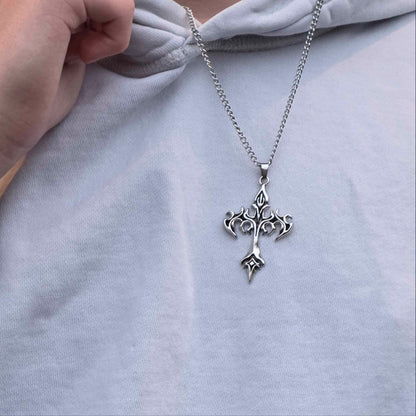 Person wearing a light gray hoodie with a silver necklace featuring a cross pendant.