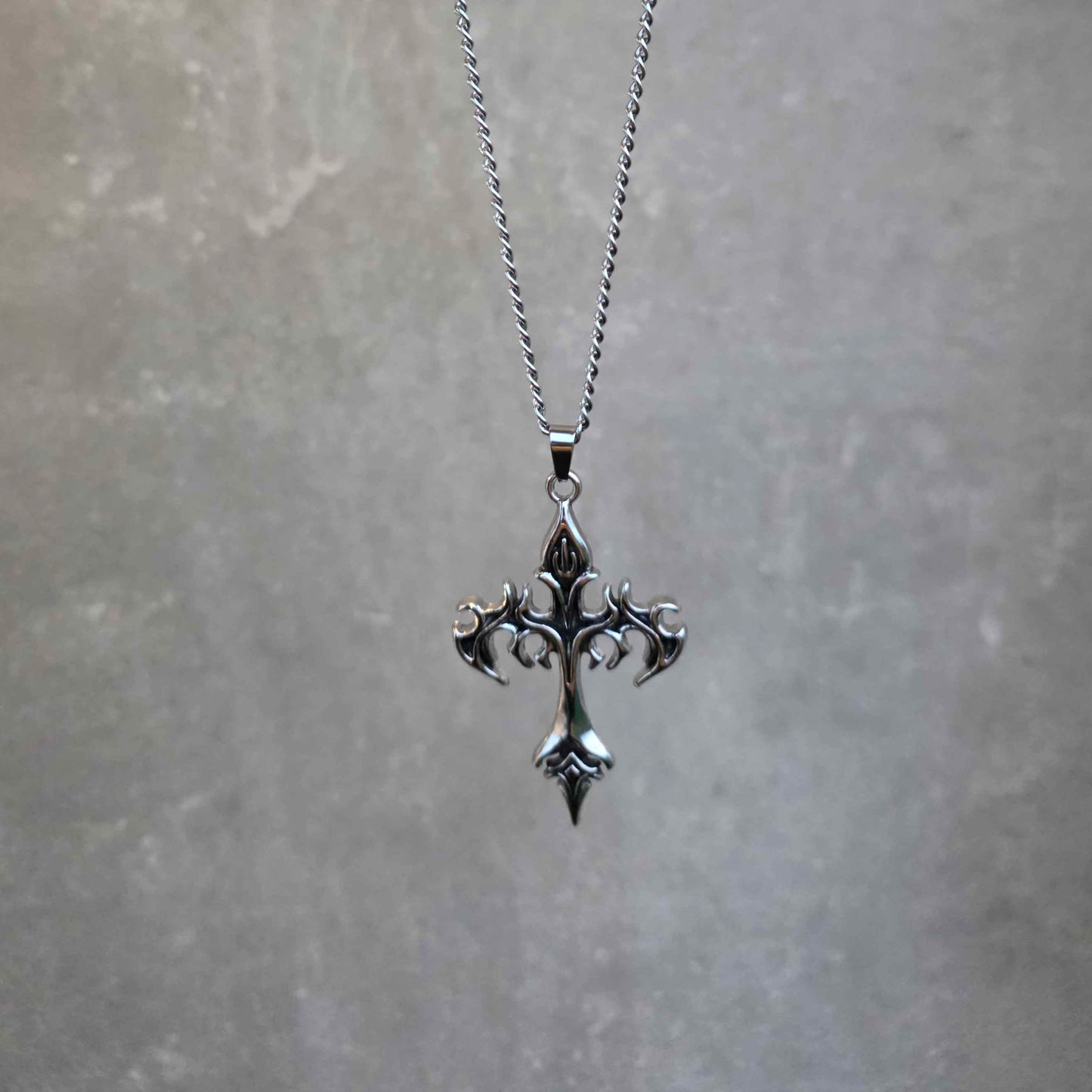 Silver cross necklace on a chain against a gray background