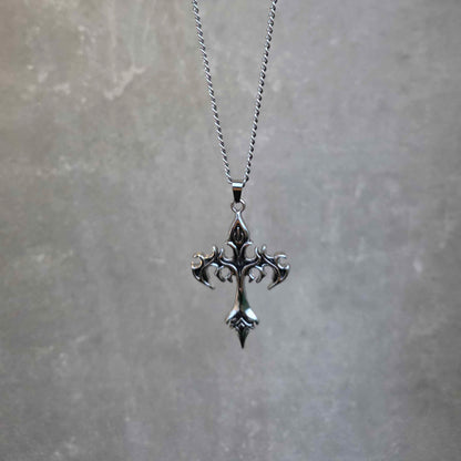 Silver cross necklace on a chain against a gray background