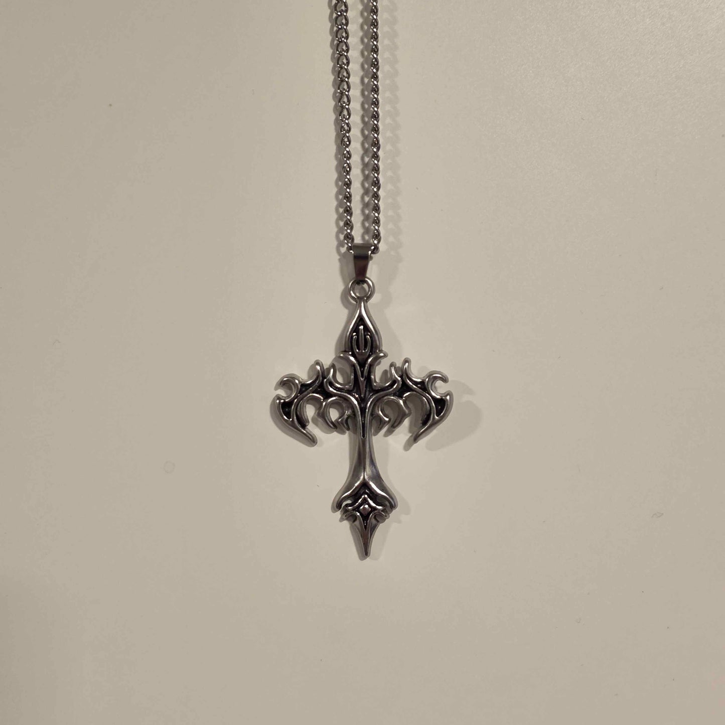 Silver cross pendant necklace on a light gray background