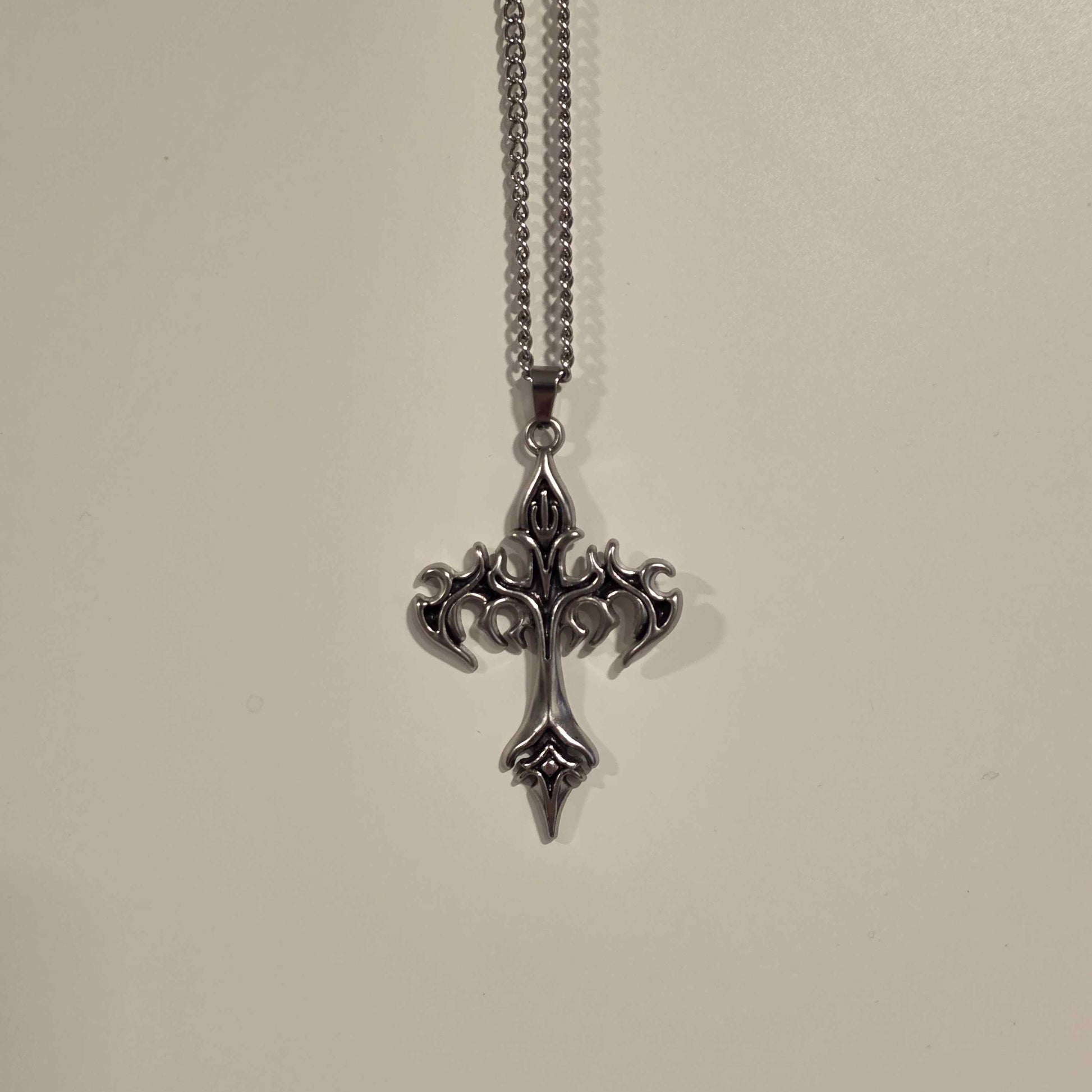 Silver cross pendant necklace on a light gray background