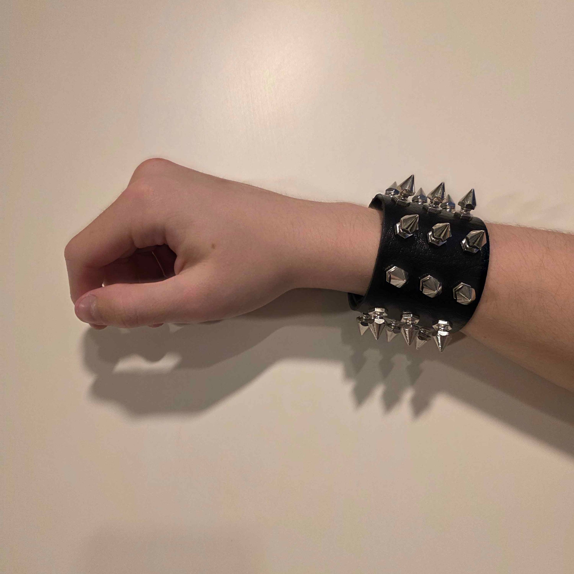 Hand wearing a black leather wristband with spikes on a plain background